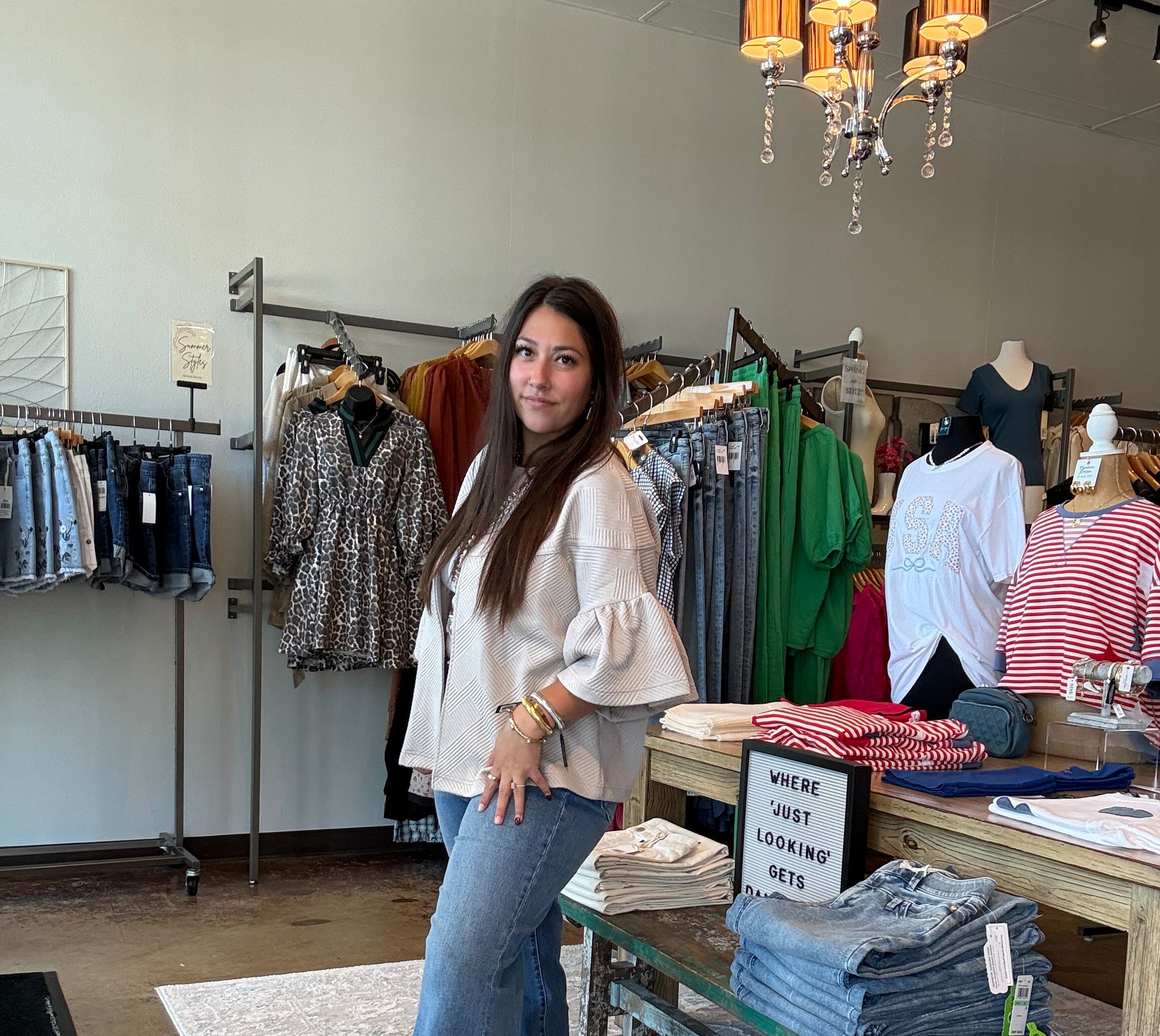 Woman standing in a clothing store with racks of clothes and a counter.