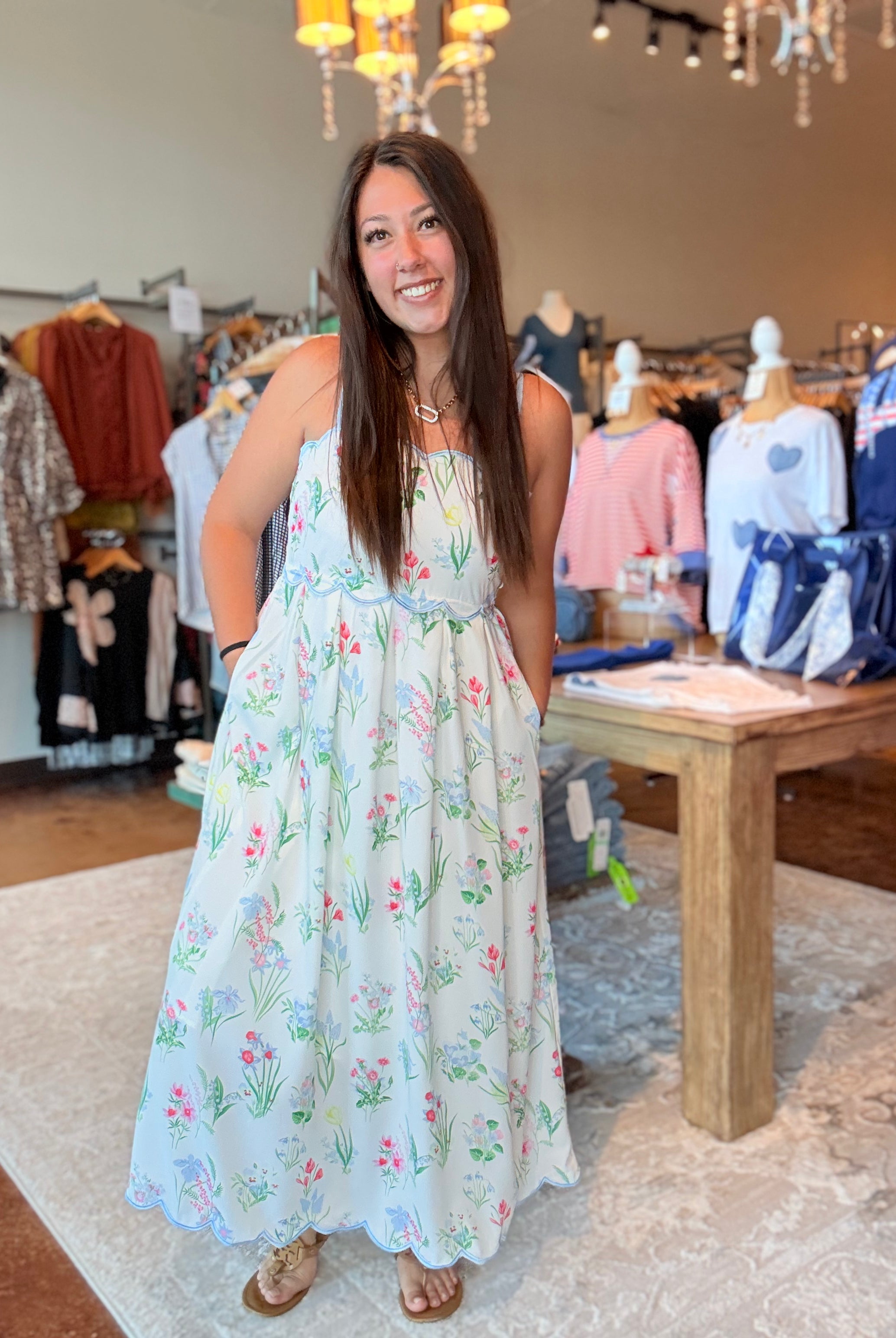 Woman in a floral dress standing in a clothing store with racks of clothes in the background.