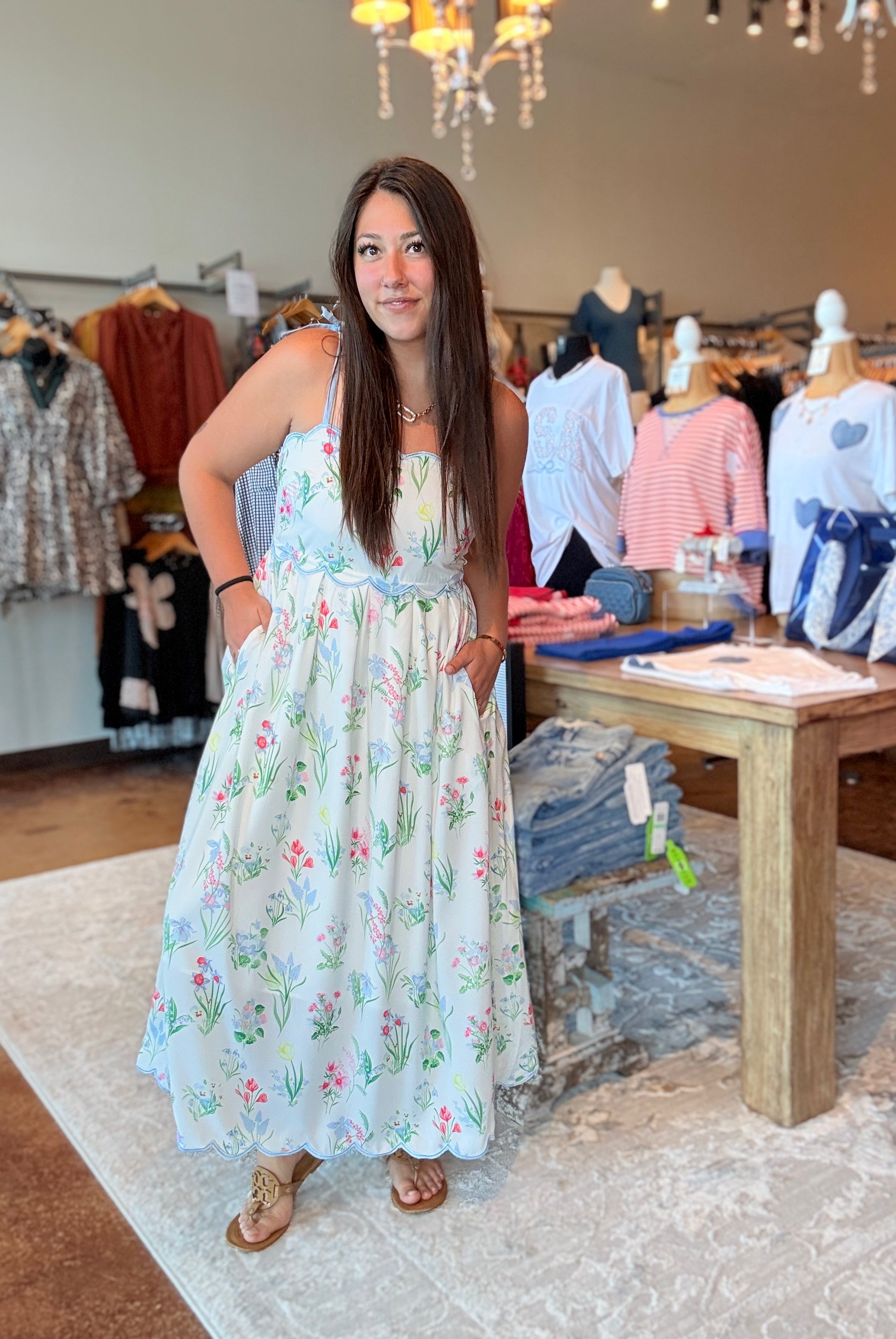 Woman in a floral dress standing in a clothing store with mannequins and clothing racks in the background.