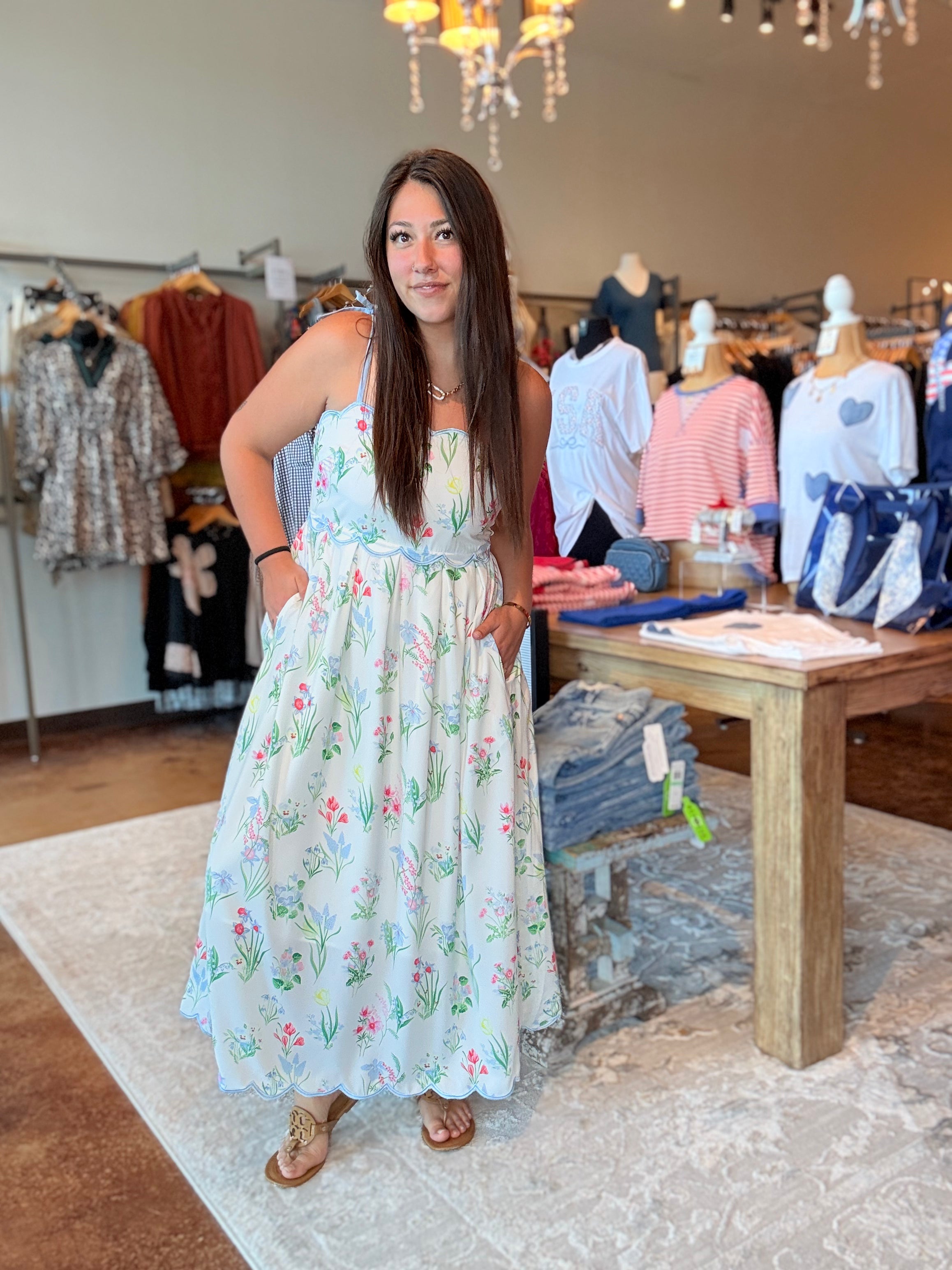 Woman in a floral dress standing in a clothing store with mannequins and clothing racks in the background.