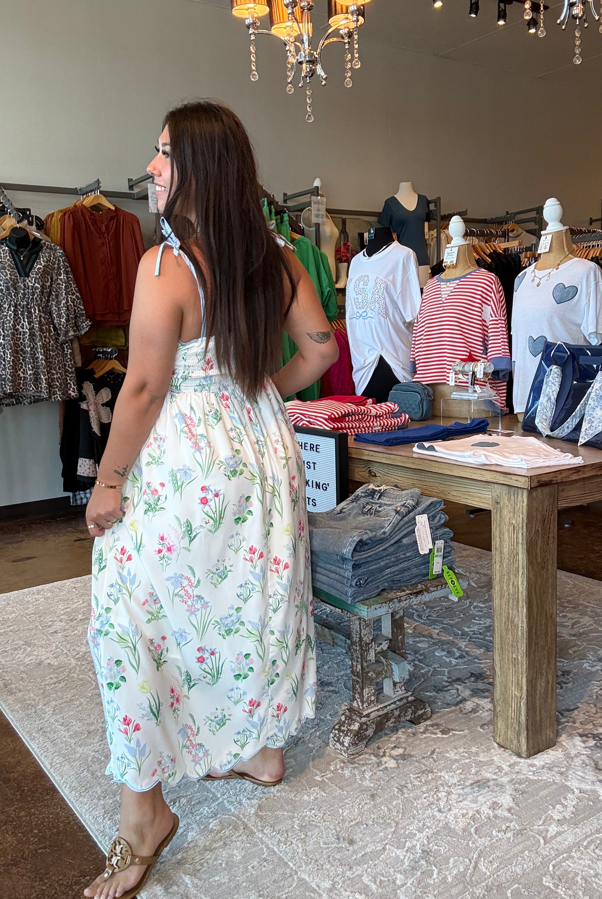Woman in a floral dress standing in a clothing store with mannequins and racks of clothes.
