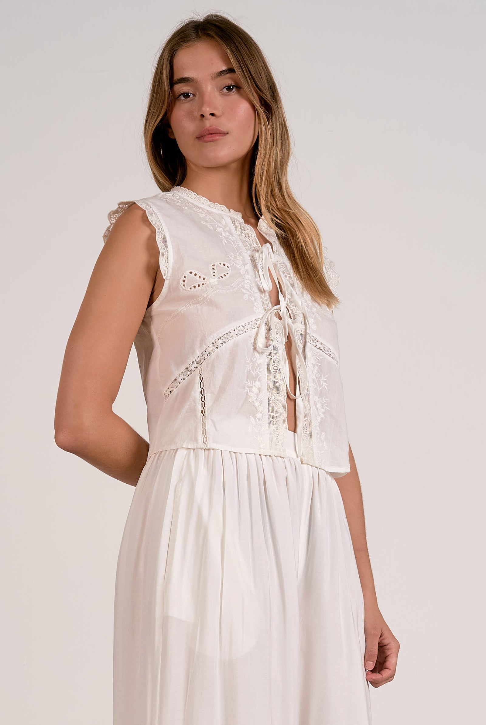 Woman wearing a white sleeveless dress with lace details on a plain background