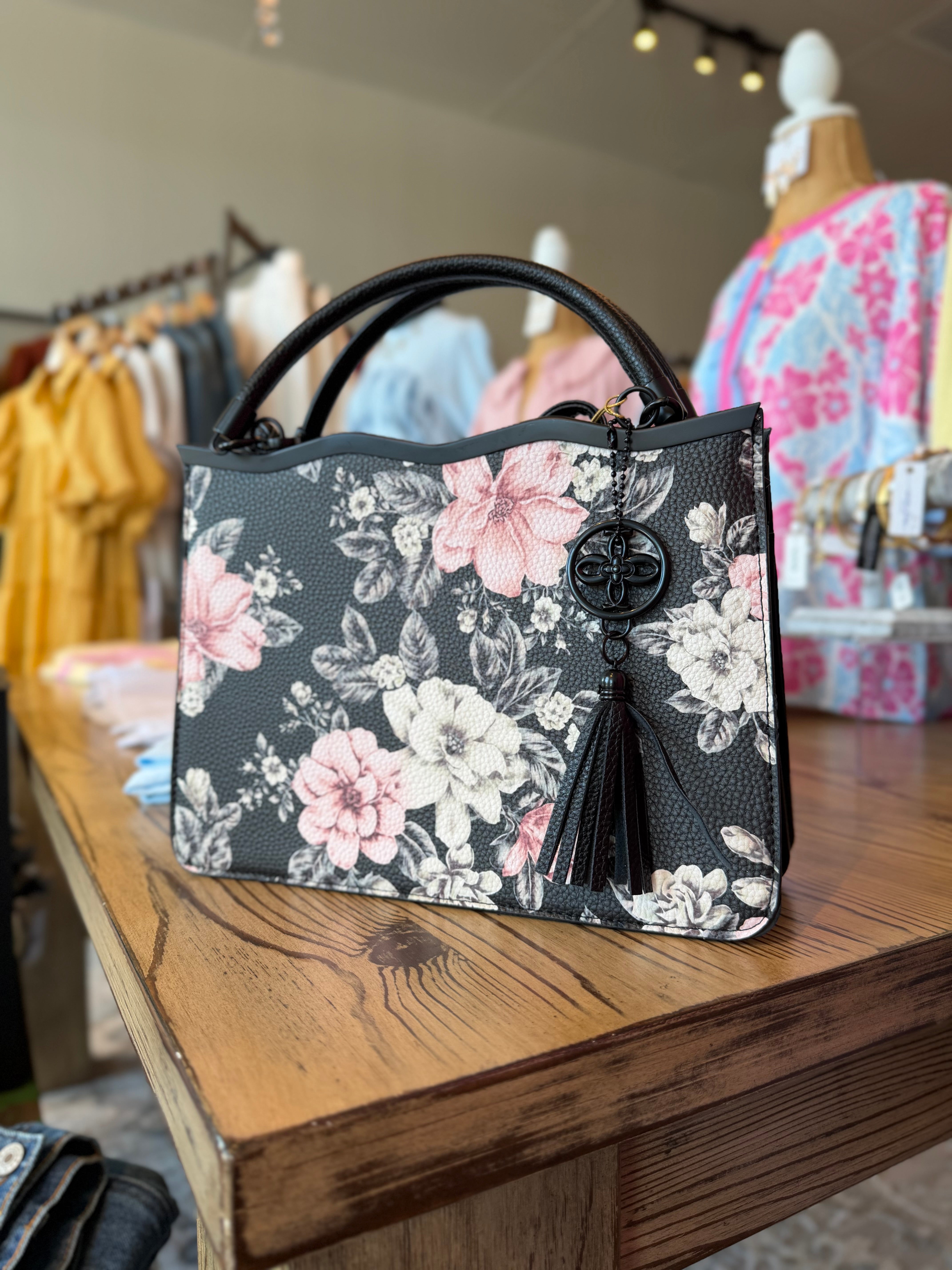 Floral-patterned handbag on a wooden surface with clothing in the background