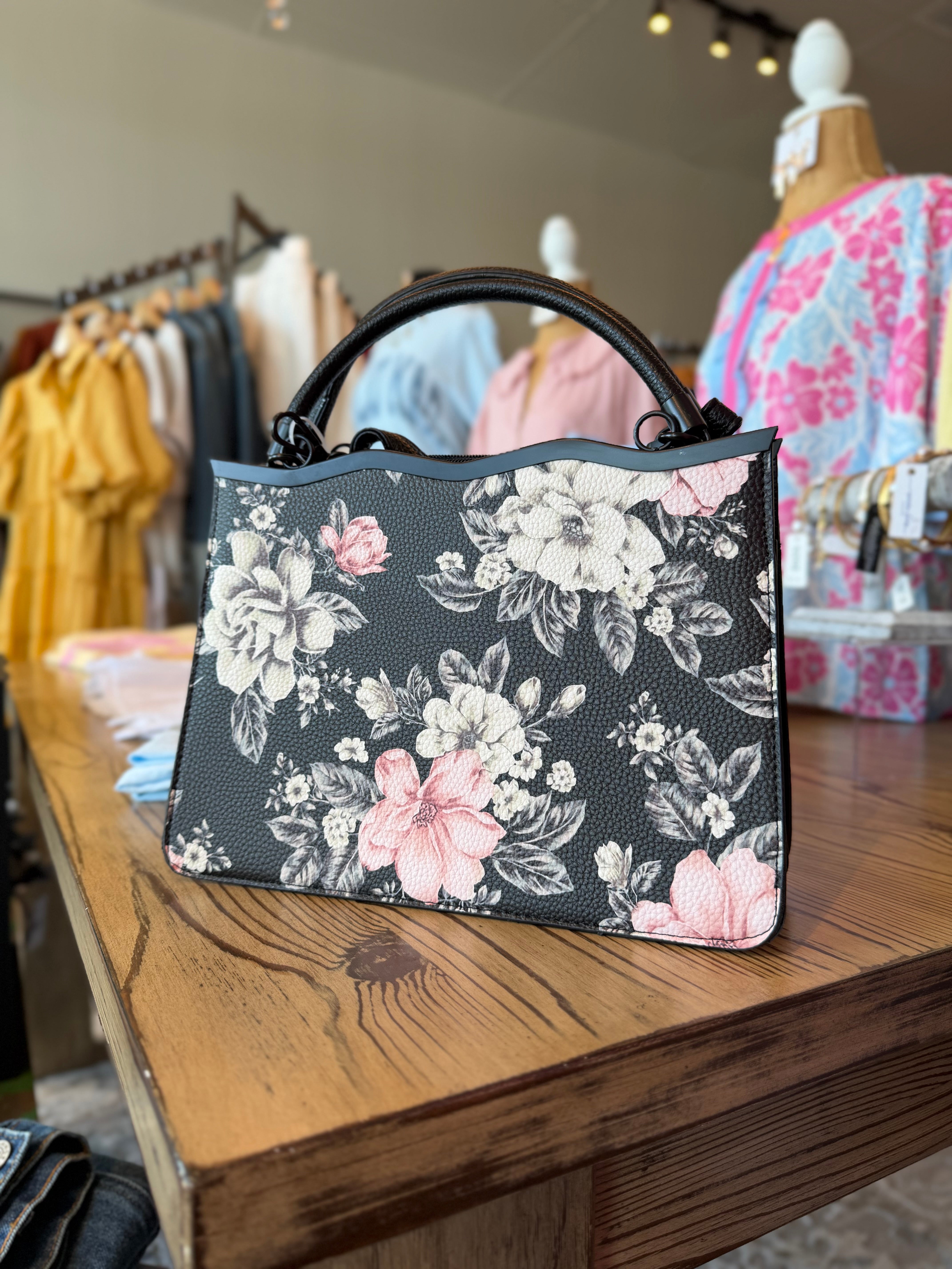 Floral-patterned handbag on a wooden surface with clothing in the background