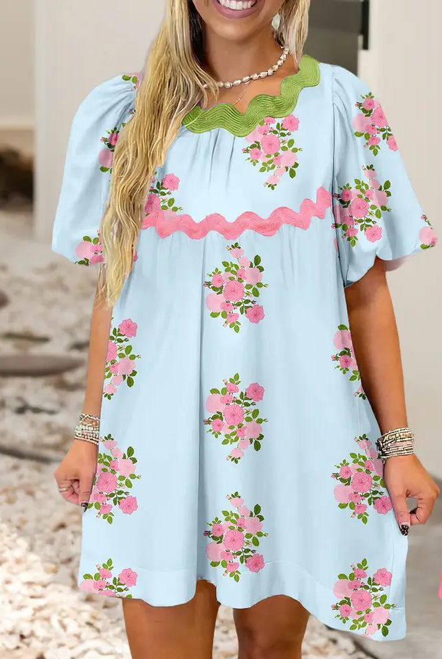 Woman wearing a light blue dress with pink floral embroidery on a neutral background