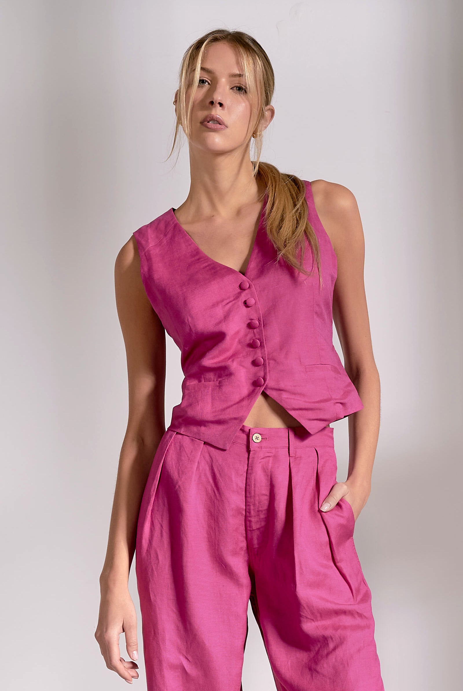 Woman wearing a pink sleeveless top and pants against a plain background