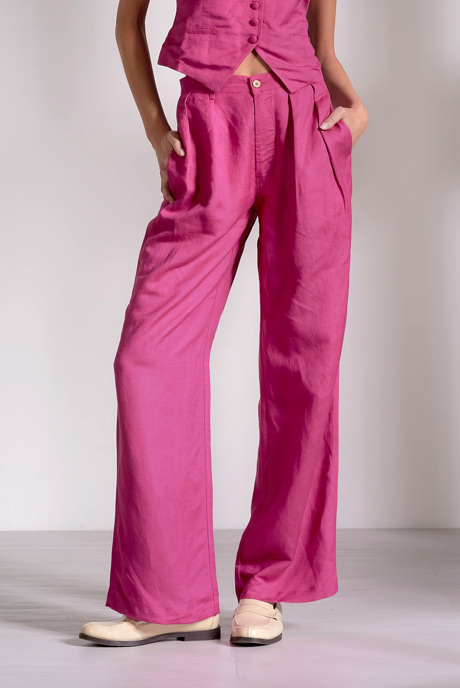 Person wearing bright pink pants and a matching top on a plain background