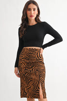 A woman modeling a black long-sleeve crop top and a brown and black tiger-print pencil skirt with a front slit, against a plain white studio background.