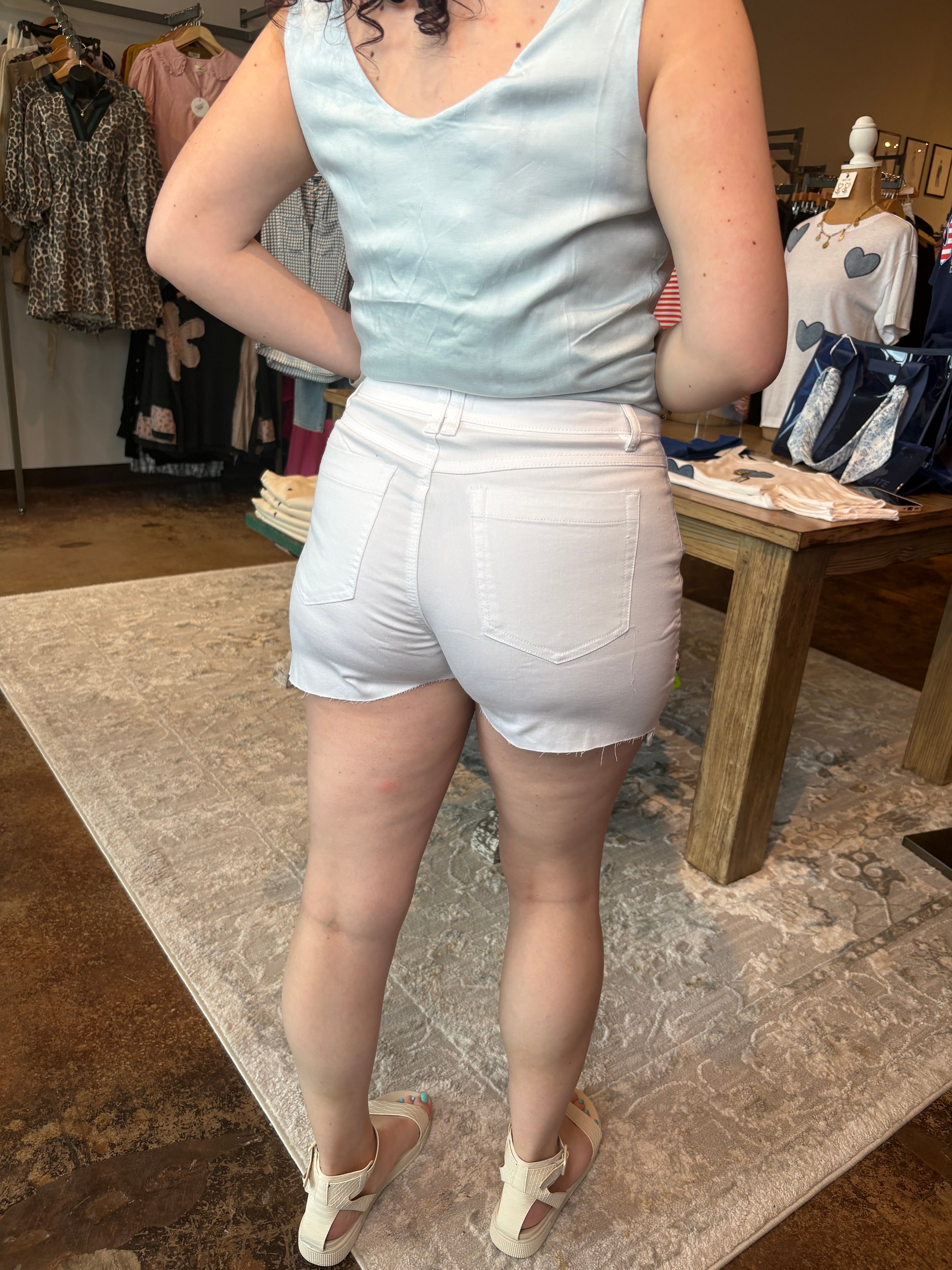 Person wearing a light blue sleeveless top and white shorts in a store setting.