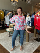 Woman posing in a clothing store wearing a floral blouse and jeans.