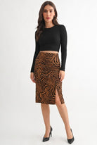 A woman modeling a black long-sleeve crop top and a brown and black zebra-print knee-length skirt with a front slit, paired with black pointed-toe heels, against a plain white studio background.