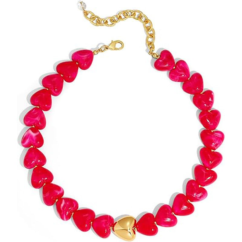 A heart-shaped beaded necklace featuring glossy hot pink heart beads with a central gold heart pendant and a gold chain extender clasp, shown on a plain white background.