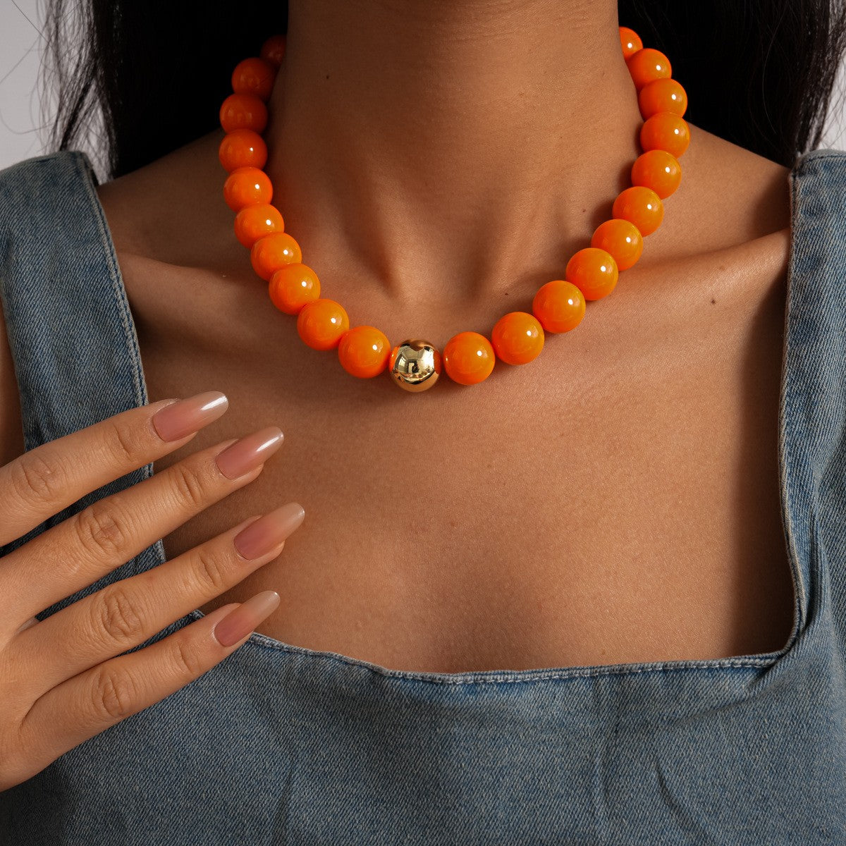 Orange beaded necklace with a gold clasp on a person wearing a denim top.