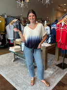 Woman standing in a clothing store wearing an ombre top and jeans.