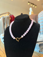 A pink beaded necklace with a gold toggle clasp displayed on a black velvet jewelry bust in a retail store setting.