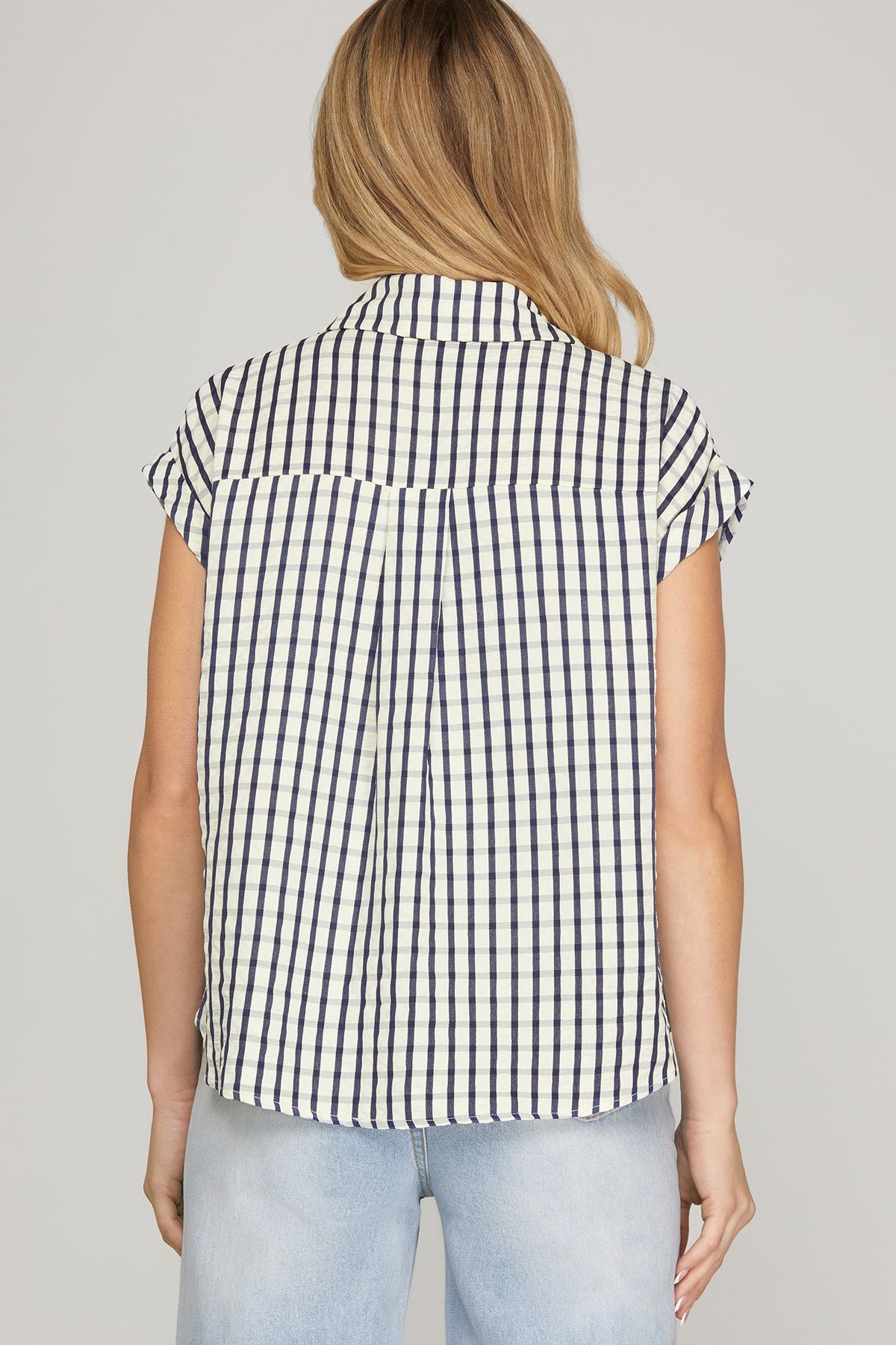 Woman wearing a black and white checkered sleeveless shirt against a plain background