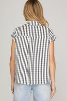 Woman wearing a black and white checkered sleeveless shirt against a plain background