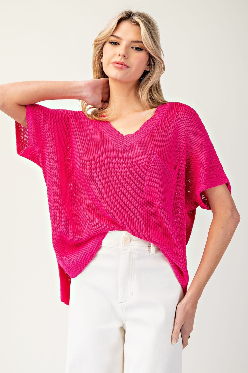 Woman wearing a bright pink sweater and white pants on a plain background