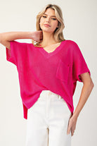 Woman wearing a bright pink sweater and white pants on a plain background