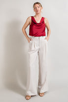 Woman wearing a red sleeveless top and white pants against a plain background