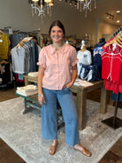 Woman in a pink shirt and blue jeans standing in a clothing store.
