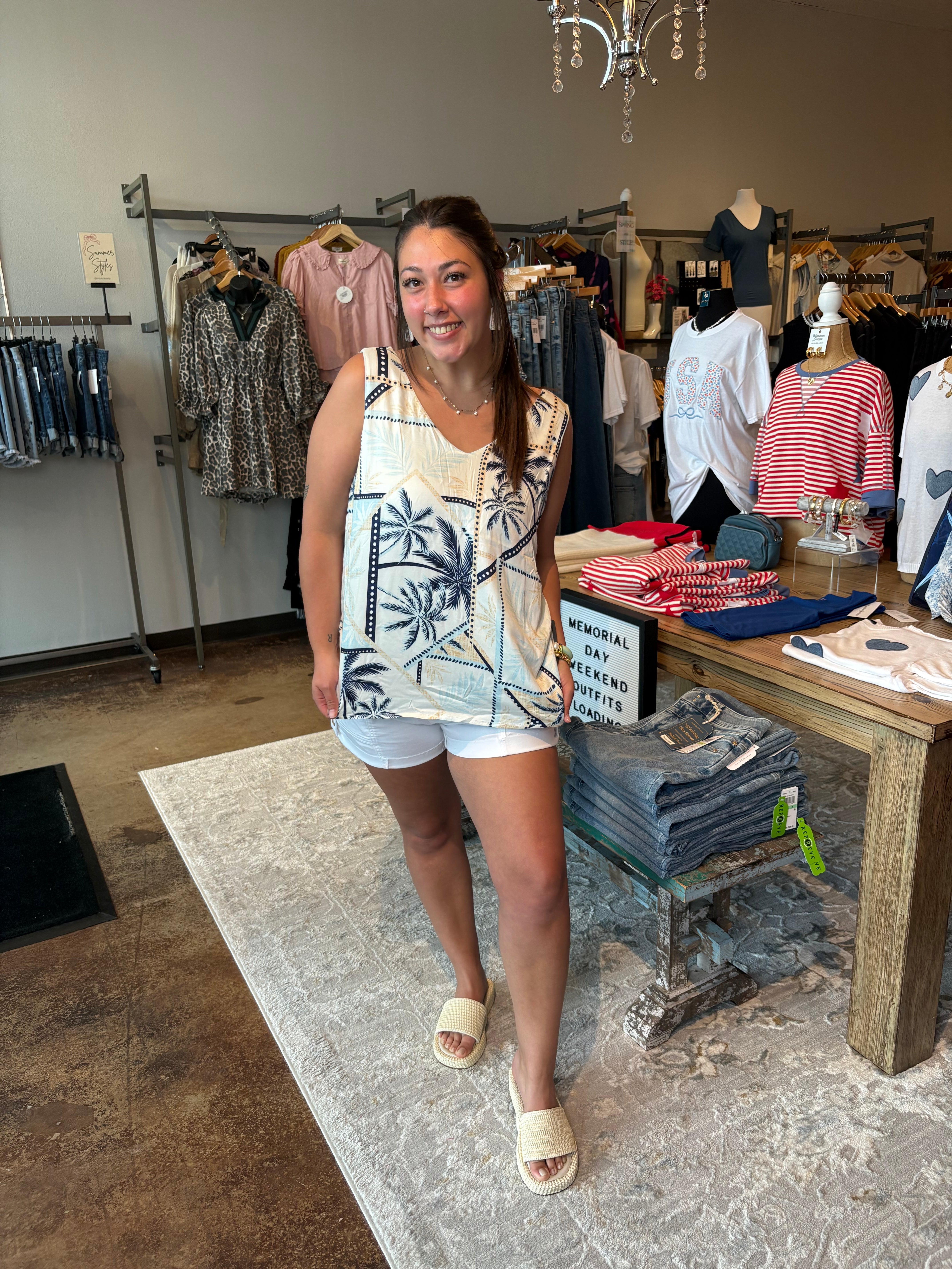 Woman standing in a clothing store wearing a sleeveless top and shorts.
