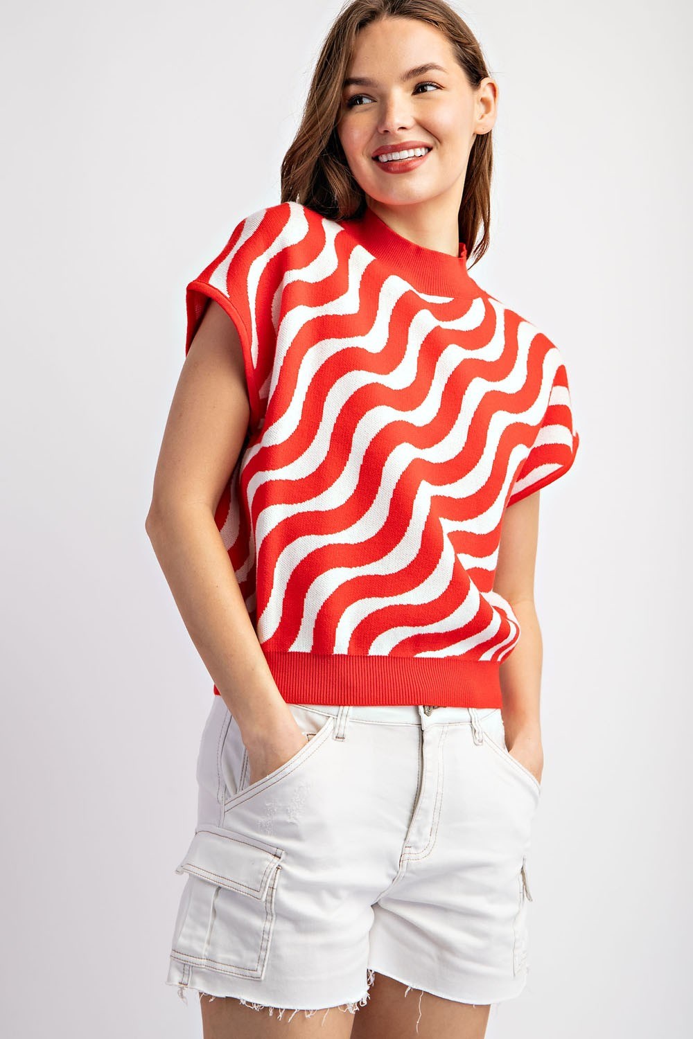 Woman wearing a red and white wavy patterned top with white shorts on a light gray background