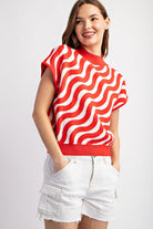 Woman wearing a red and white wavy patterned top with white shorts on a light gray background