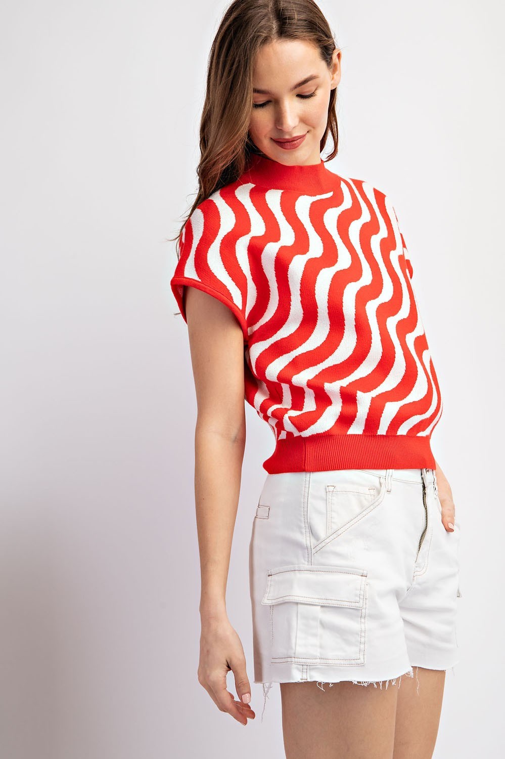 Woman wearing a red and white patterned top with white shorts on a light gray background