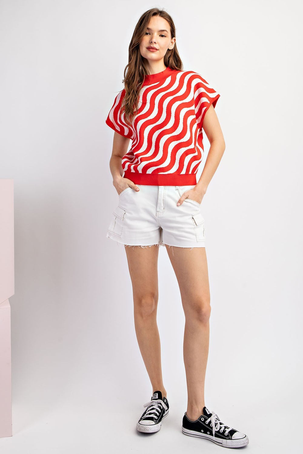 Woman wearing a red and white striped shirt with white shorts on a light gray background