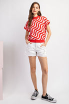 Woman wearing a red and white striped shirt with white shorts on a light gray background