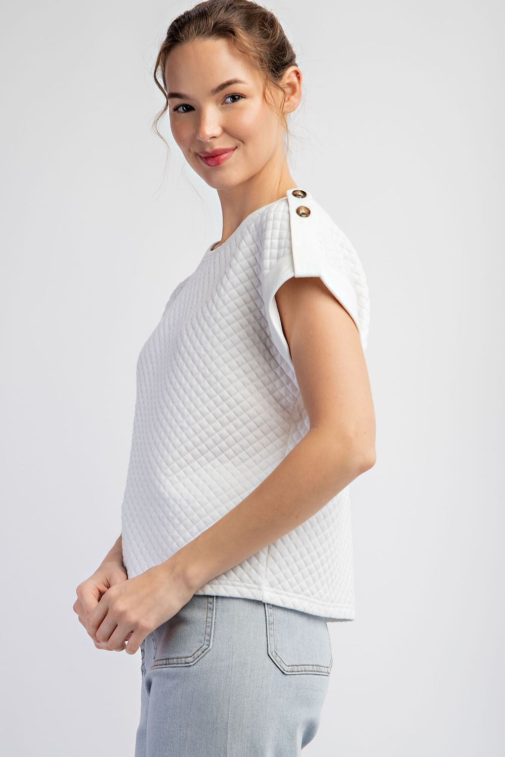 Woman wearing a white textured top and light blue jeans on a plain background