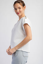 Woman wearing a white textured top and light blue jeans on a plain background