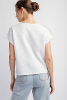 Woman wearing a textured white top and light blue jeans on a plain background