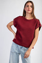 Woman wearing a textured red top and light blue jeans on a white background