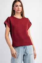 Woman wearing a textured red top and light blue jeans on a white background