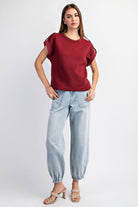 Woman wearing a red textured top and light blue jeans on a white background
