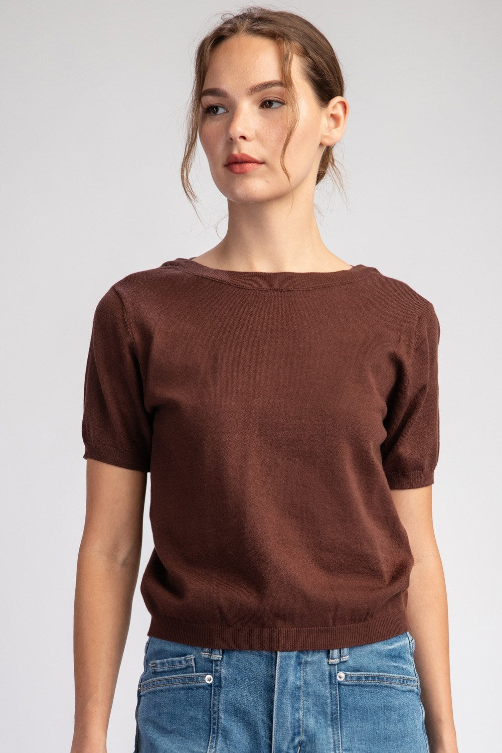 Woman wearing a brown sweater and blue jeans against a plain background