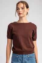 Woman wearing a brown sweater and blue jeans against a plain background