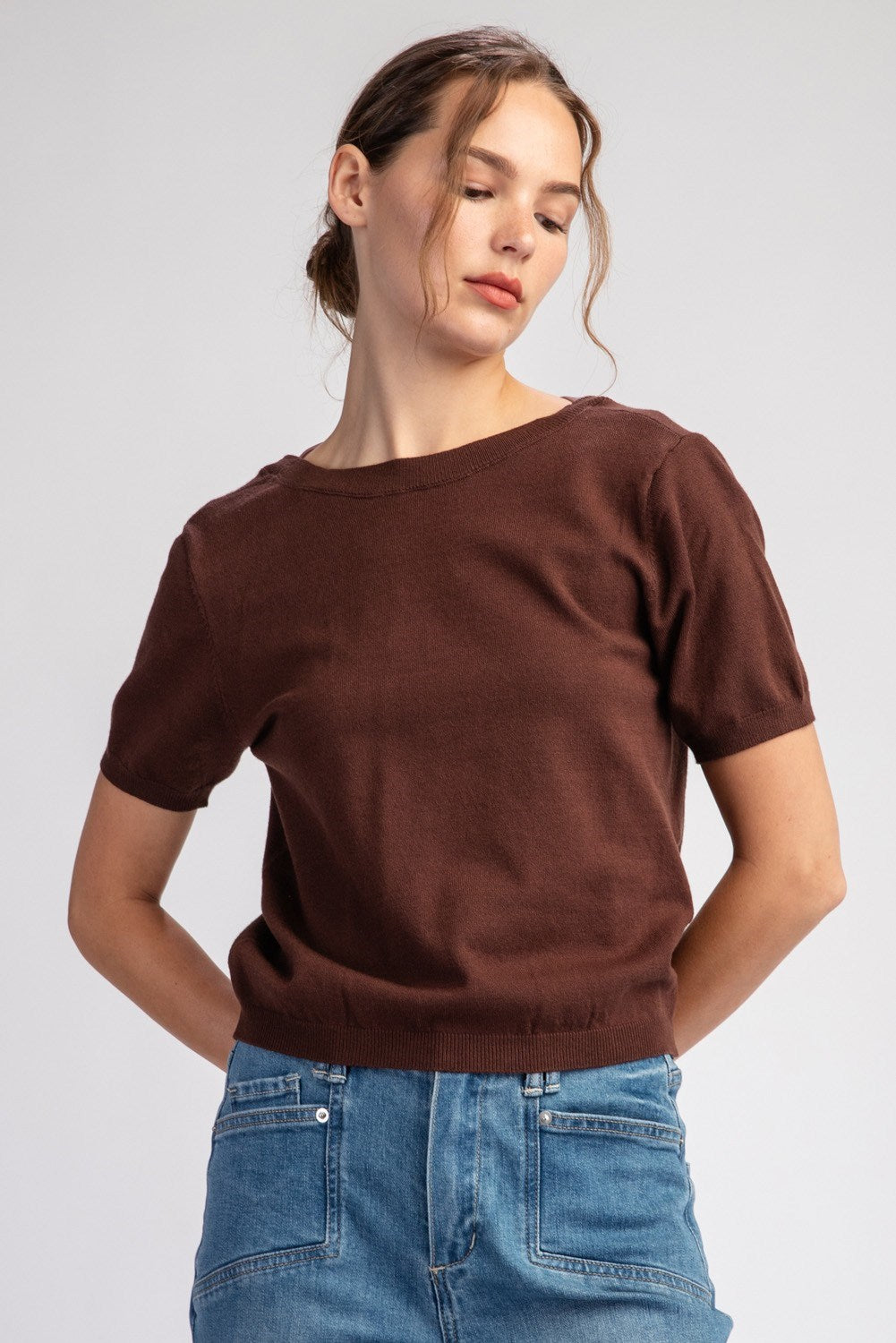 Woman wearing a brown sweater and blue jeans on a light gray background