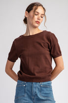 Woman wearing a brown sweater and blue jeans on a light gray background