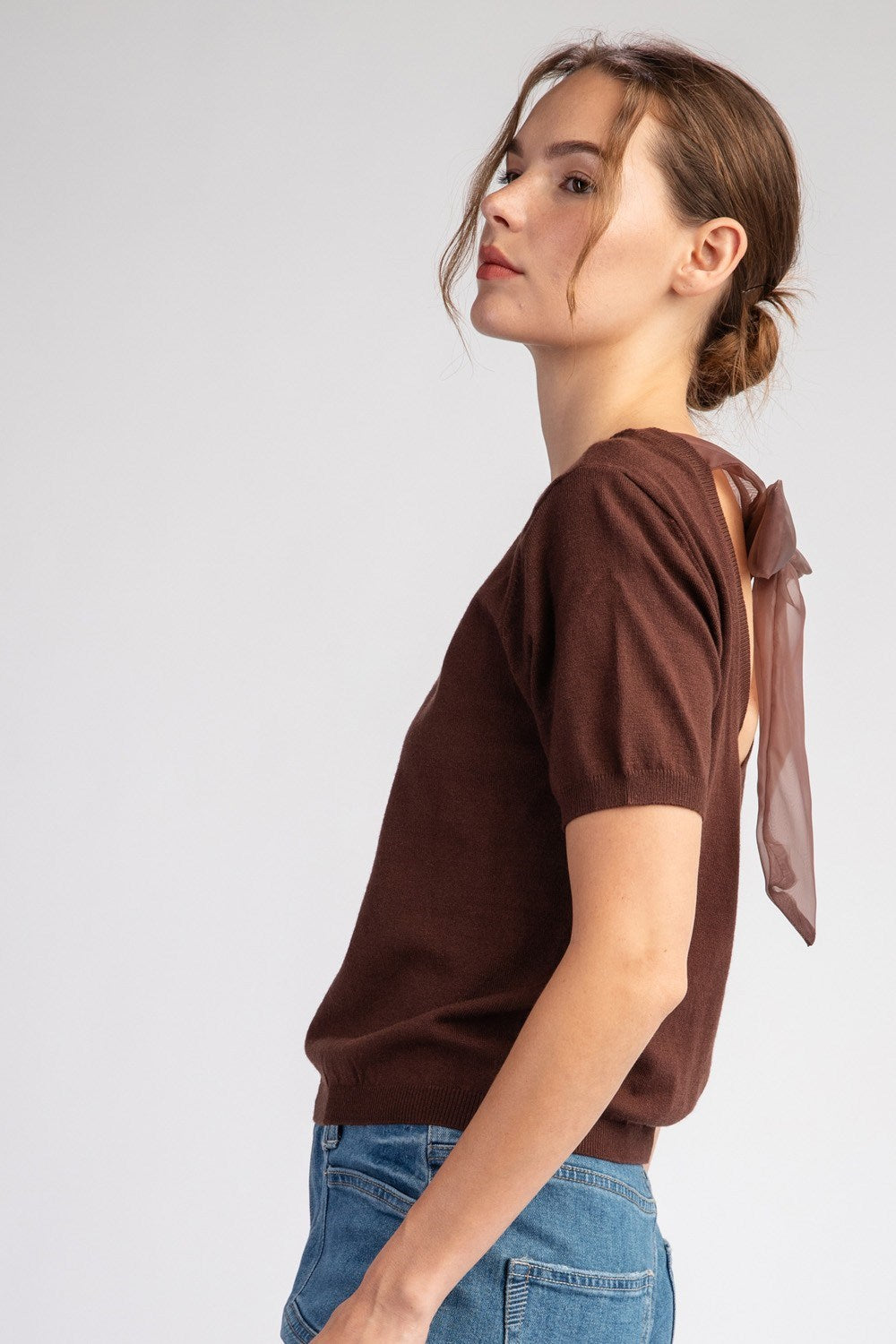 Woman wearing a brown t-shirt with a bow detail on a plain background