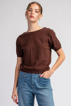 Woman wearing a brown top and blue jeans on a plain background