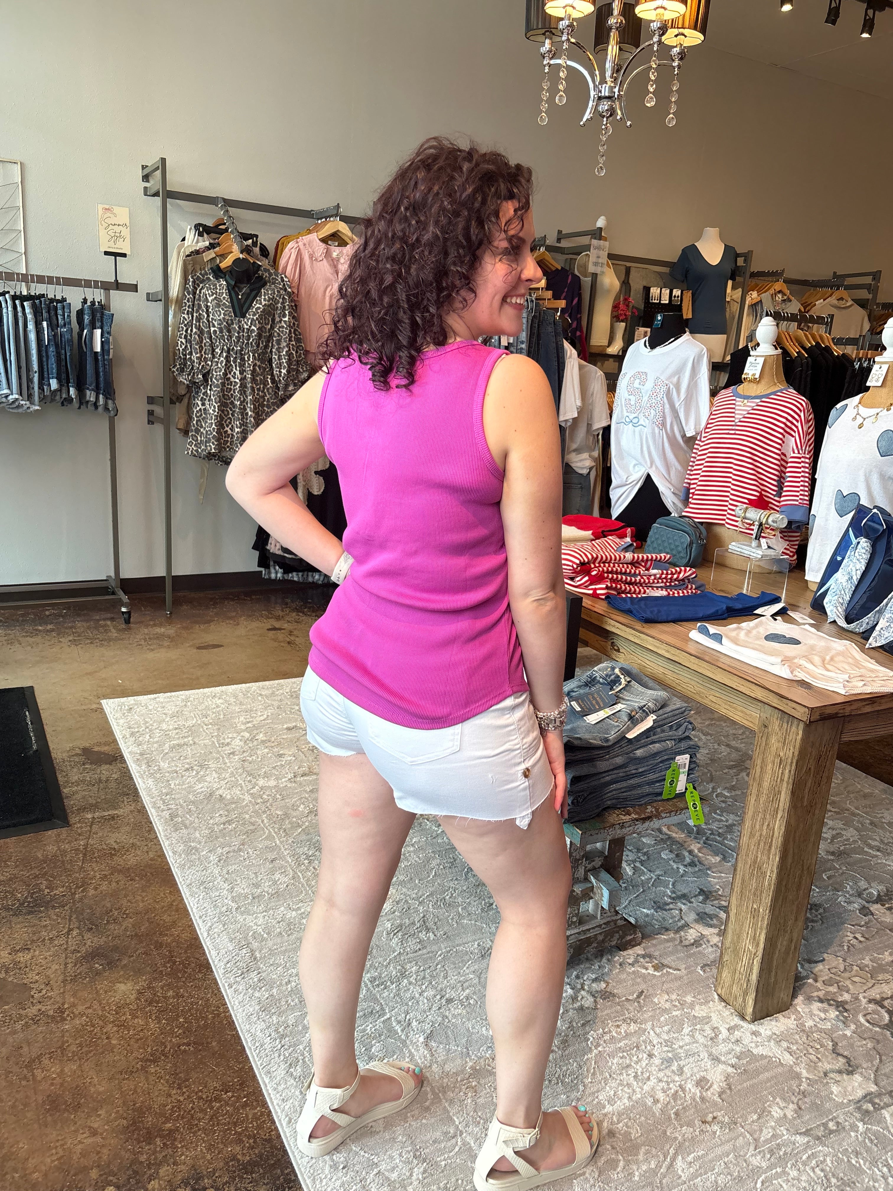 Woman in a pink top and white shorts standing in a store with clothes on racks.