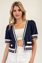 Woman wearing a navy cardigan with white trim on a plain background