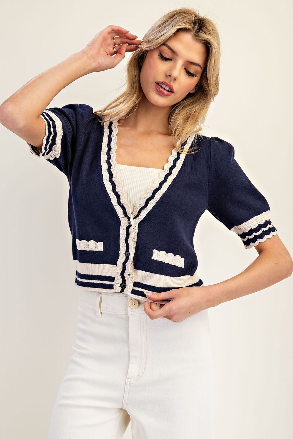 Woman wearing a navy cardigan with white trim on a plain background