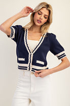 Woman wearing a navy cardigan with white trim on a plain background