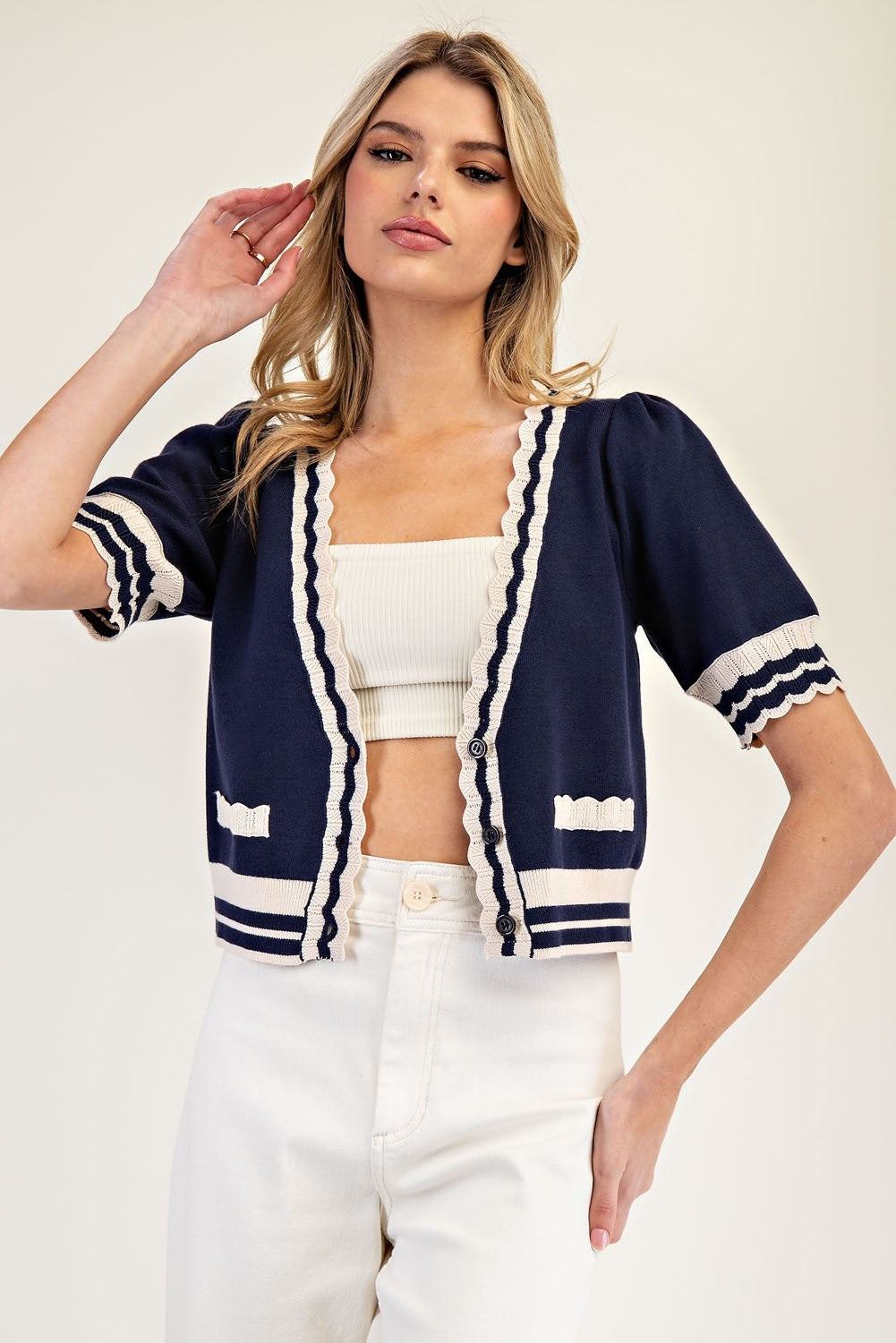 Woman wearing a navy cardigan with white trim on a plain background