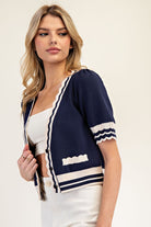 Woman wearing a navy cardigan with white trim on a plain background