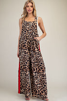 A woman modeling a leopard-print sleeveless jumpsuit with wide legs and red side panels, photographed against a plain light beige studio background.